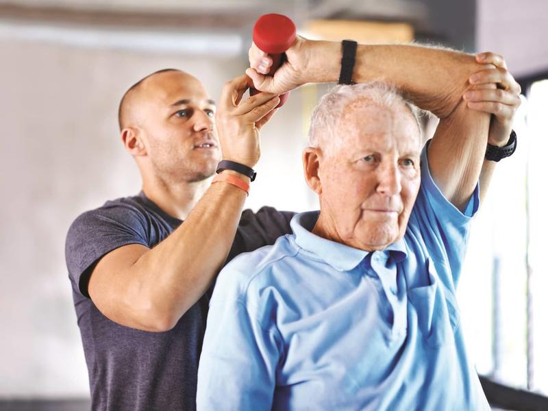 elderly male working with a physical therapist lifting weights