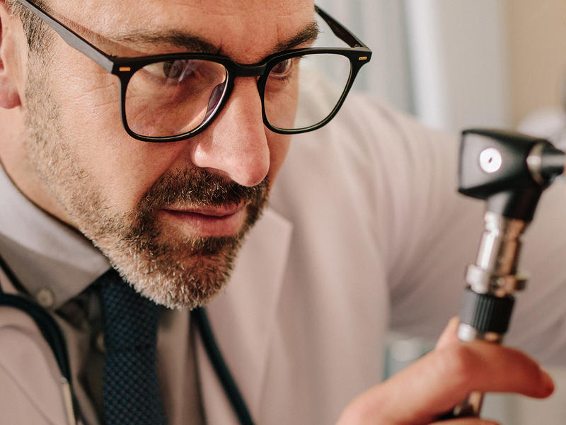 Doctor in white lab coat uses otoscope to examine ear of patient