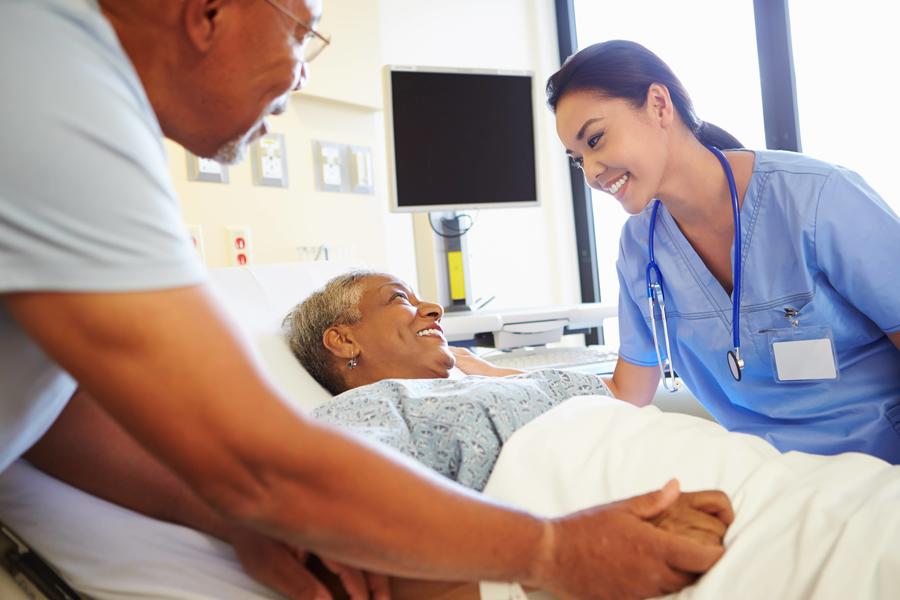 Healthcare professional smiles at patient in hospital bed