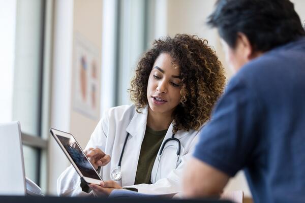 Woman doctor showing man an image on tablet.