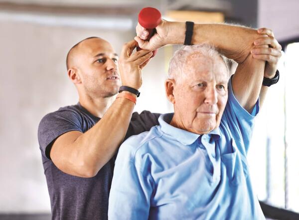 elderly male working with a physical therapist lifting weights