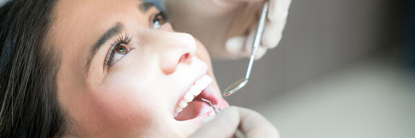 Patient reclined with open mouth and gloved hands utilizing dental instruments