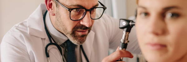 Doctor in white lab coat uses otoscope to examine ear of patient