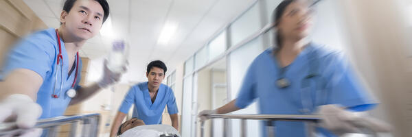 Team of blue clad hospital clinicians are transporting gurney along hospital corridor